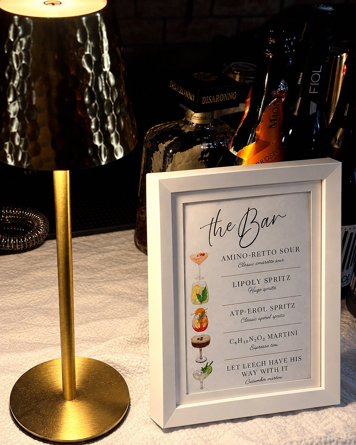 A framed Liquor N Ice cocktail menu on the bar beside a brass lamp and bottles